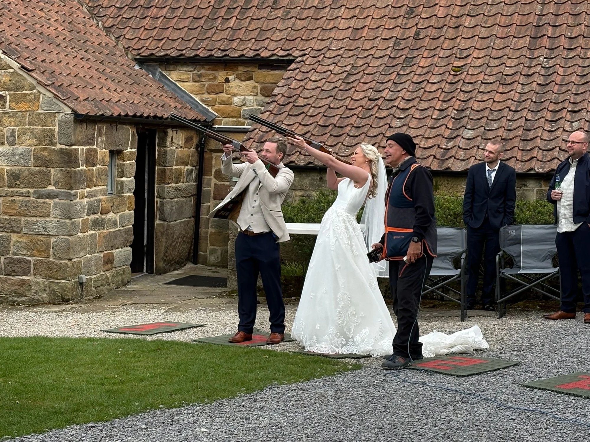 Bride taking a shot at a laser clay stand outside a stone church